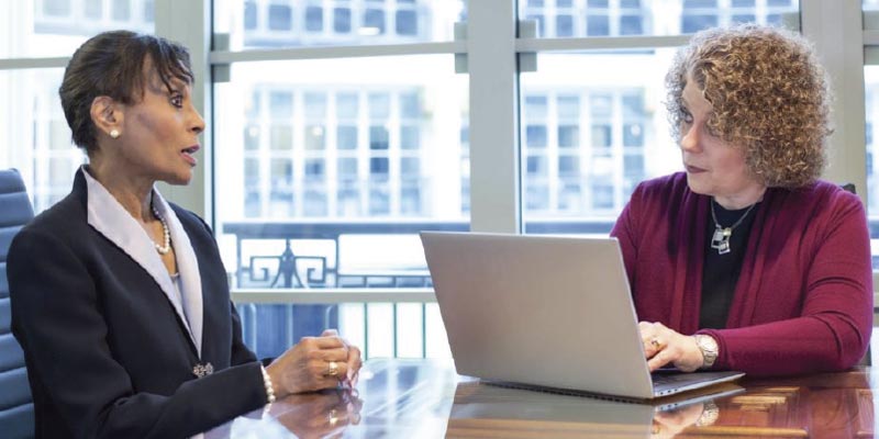Teresa Zumwald speaking with a female client, while typing on a laptop.