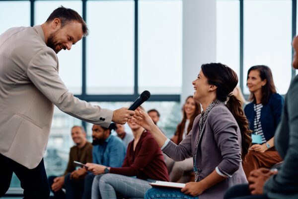 Happy presenter interacting with the audience during business seminar in conference hall.