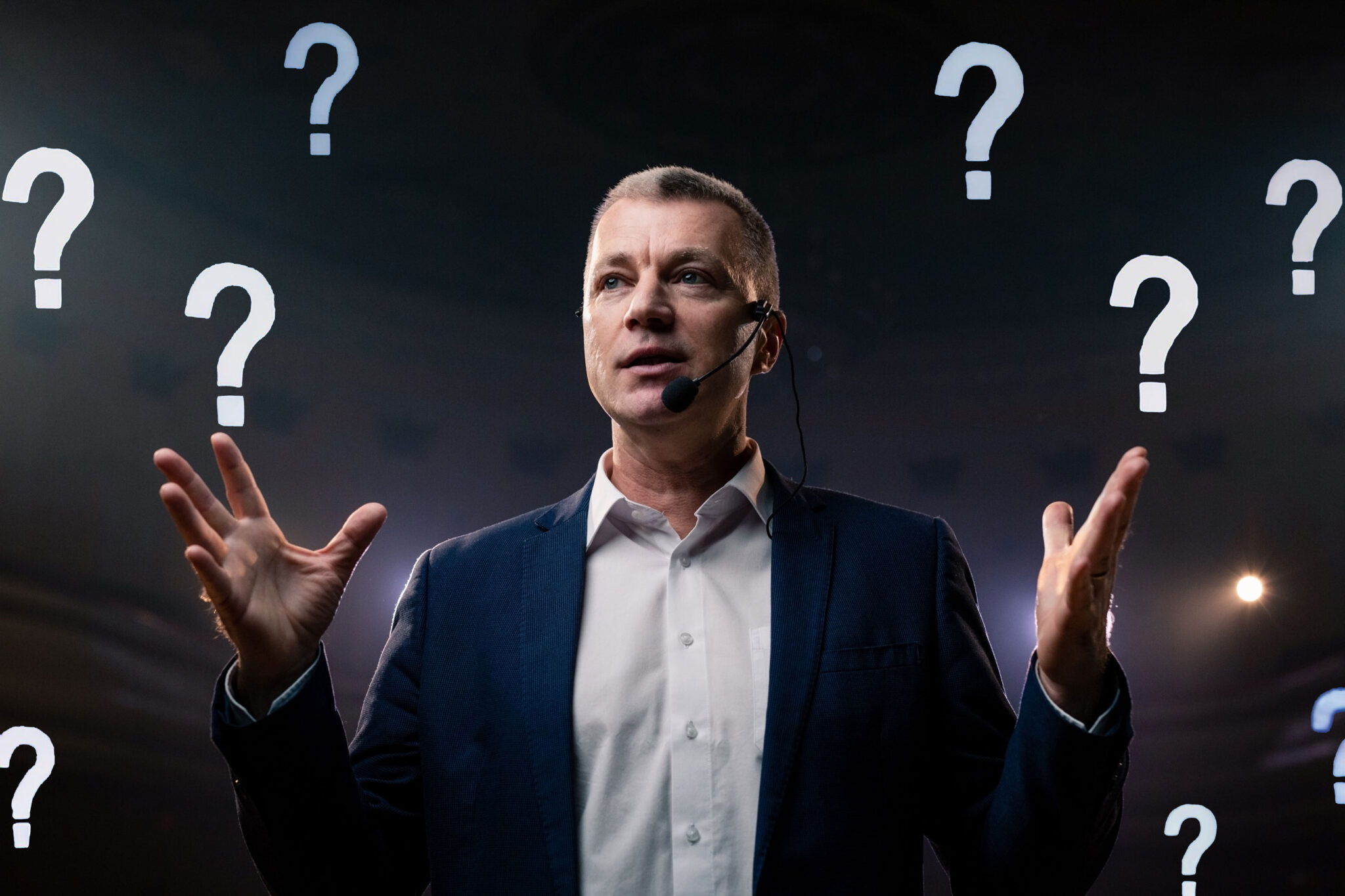 Male speaker with question marks around him.