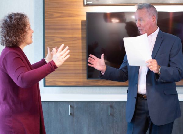 Teresa Zumwald, with arms outstretched, enthusiastically speaking with another business professional.