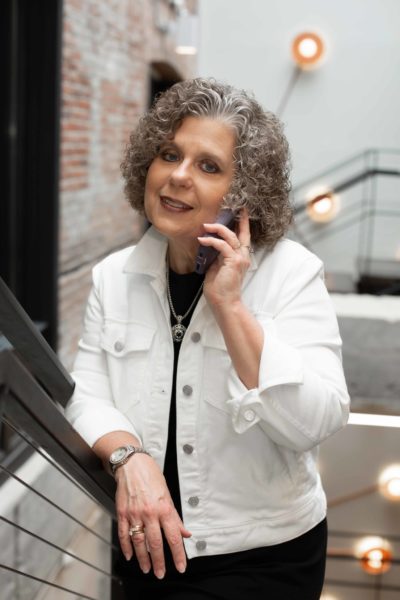 Teresa Zumwald looking professional, dressed in business attire, making direct eye contact with the camera while holding a phone to her ear.