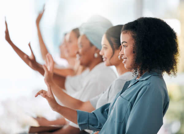 Several women looking in the same direction with all of their hands lifted up high.