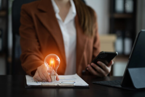 Business woman holding a light bulb in one hand and a cellphone in the other, in an office setting