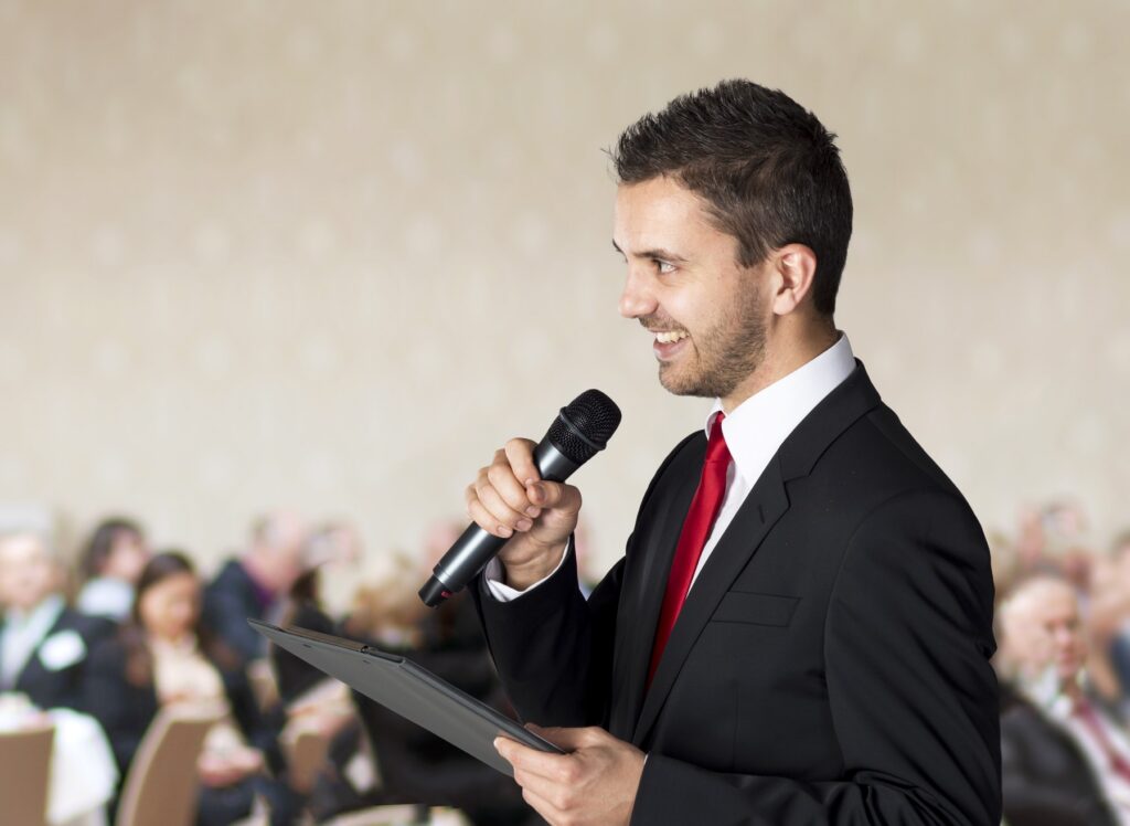 Businessman in a suit speaking into a microphone and engaging a group