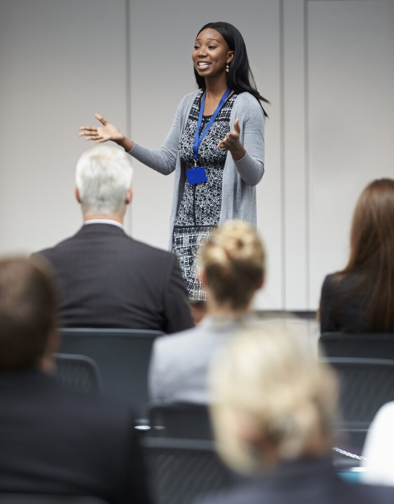 Young businesswoman speaking confidently to a group of professionals in a conference setting