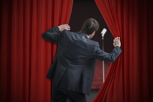 Nervous man is afraid of public speech and is hiding behind curtain.