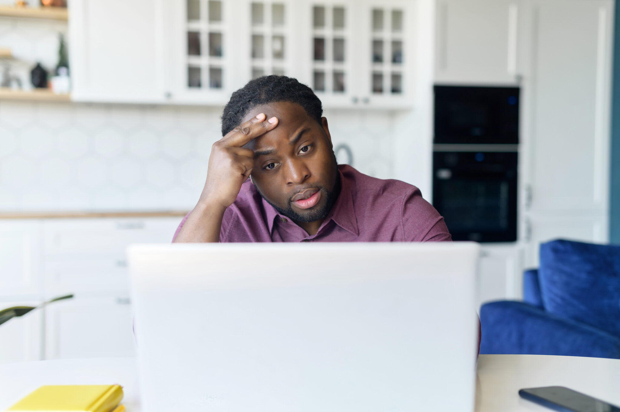 Worried African-American male using laptop for remote work from home, watching weary at the screen